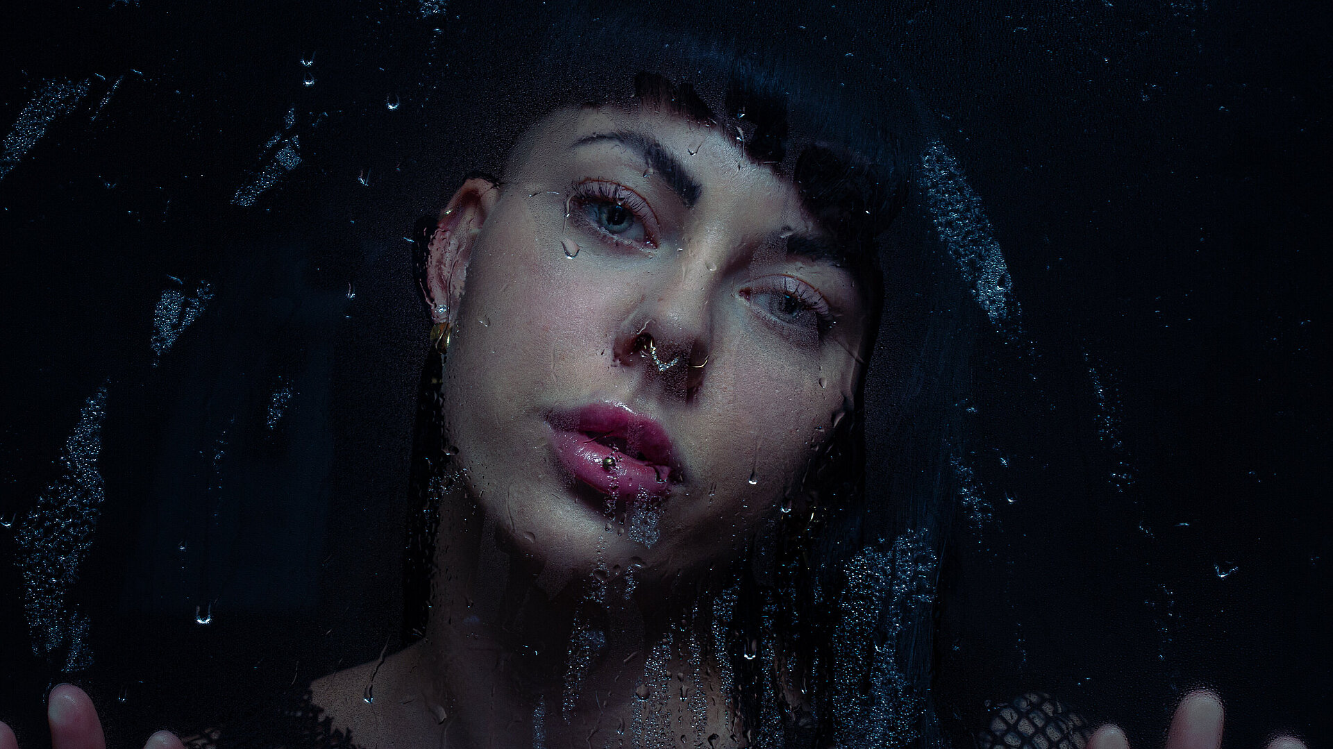 Woman on dark background behind a rainy window.